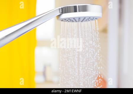 Nahaufnahme von fließenden Wassertropfen aus einem Duschkopf in einem hellen Badezimmer mit Fenster im Hintergrund Stockfoto