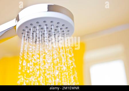 Nahaufnahme fließender Wassertropfen aus einem Duschkopf in einem hellen Badezimmer mit gelbem Hintergrund Stockfoto