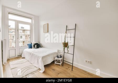 Ein Schlafzimmer mit weißen Wänden und Hartholzfußboden im Zimmer, es gibt eine Leiter an der Wand Stockfoto