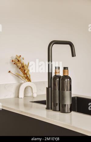 Ein Waschbecken mit zwei Wasserhähnen und eine Vase auf dem Tresen daneben vor einer weißen Wand Stockfoto