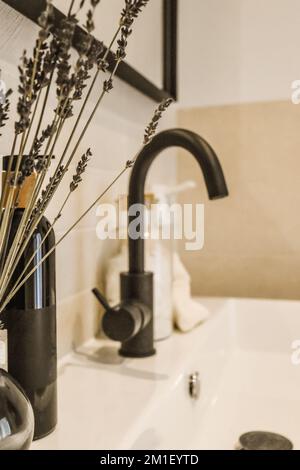 Ein paar Blumen in einer Vase auf einem Waschbecken im Badezimmer mit Seife und Zahnbürsten neben dem Wasserhahn Stockfoto