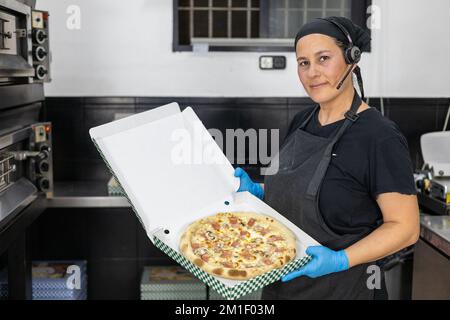 Weibliche Chefköchin mit frisch zubereiteter Pizza in einer Schachtel zum Mitnehmen Stockfoto