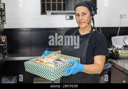 Weibliche Chefköchin mit frisch zubereiteter Pizza in einer Schachtel zum Mitnehmen Stockfoto