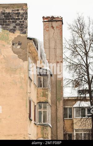 Lange, vereiste Eiszapfen hängen im Frühling oder Winter am Dachrand. Wand eines alten Backsteinhauses mit Fenstern. Große Eiszapfen in glatten, schönen Reihen. Bewölkter Wintertag, weiches Licht. Stockfoto