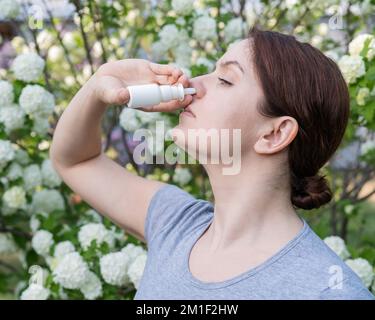 Kaukasische Frau verwendet ein Nasenspray, während sie im Park spazieren geht. Stockfoto
