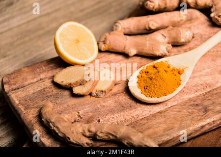 Nahaufnahme Kurkuminpulver in Holzlöffel mit frischem Rhizom auf Holzhintergrund Stockfoto