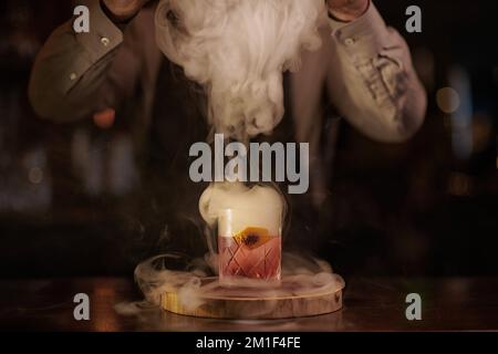 Ein köstlicher Negroni-Rauchercocktail in einem Glas, den der Barkeeper mit einem Rauchglas bedeckt Stockfoto