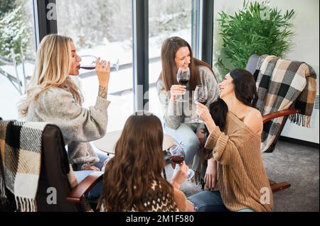 Junge Frauen genießen Winterwochenenden im modernen Scheunenhaus. Vier Mädchen, die Spaß haben und Rotwein trinken. Stockfoto