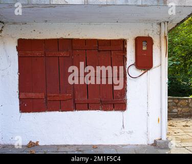 Ein rotes Holzfenster und ein elektrischer Zähler an einer alten weißen Wand. Stockfoto