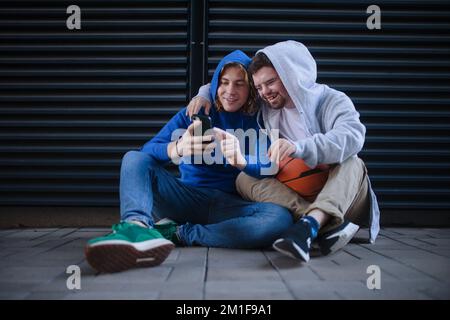 Ein Mann mit Down-Syndrom ruht sich aus, während er mit seinem Freund im Freien spielt. Freundschafts- und Integrationsbegriff für Behinderte Stockfoto