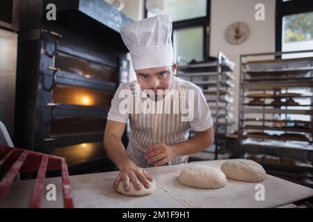 Junger Bäcker mit Down-Syndrom, der Gebäck in der Bäckerei herstellt. Konzept der gesellschaftlichen Integration von Menschen mit Behinderungen. Stockfoto