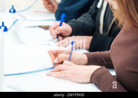 Frau füllt am Tisch ein leeres Bewerbungsformular aus oder unterzeichnet Vertrag. Hände von Menschen mit Nahaufnahme-Füllfederhalter. Perspektivische Ansicht mehrere Personen füllen Daten gleichzeitig mit einem Stift auf Papier aus. Stockfoto