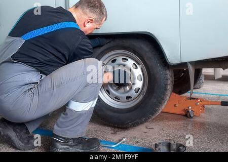 Der Mensch wechselt im Autodienst das Rad. Professioneller Automechaniker im Overall entfernt das Rad aus dem Lkw in der Garage. Authentischer Workflow... Stockfoto