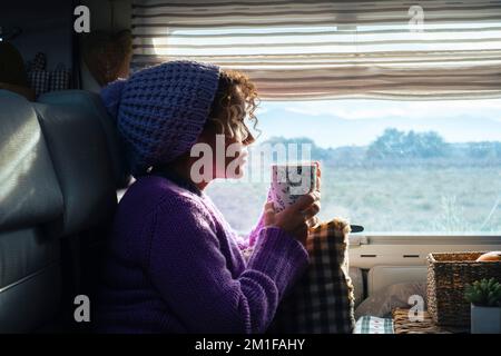 Seitenansicht einer Frau, die Kräutertee trinkt und sich in ihrem Wohnmobil entspannen und die Landschaft auf dem Parkplatz betrachten kann. Reise-Noma Stockfoto