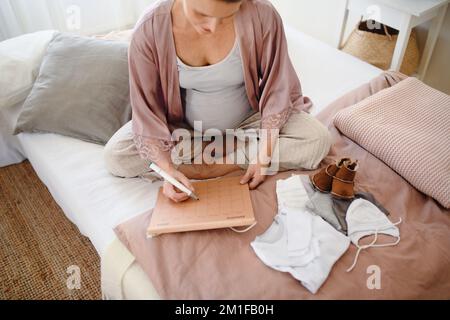 Ein Blick aus einem großen Winkel auf eine schwangere Frau, die ihr Fälligkeitsdatum im Kalender markiert. Stockfoto