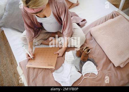 Ein Blick aus einem großen Winkel auf eine schwangere Frau, die ihr Fälligkeitsdatum im Kalender markiert. Stockfoto