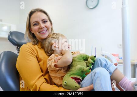 Porträt einer jungen Mutter mit ihrer kleinen Tochter, die im Zahnarztstuhl in seinem Büro sitzt. Stockfoto