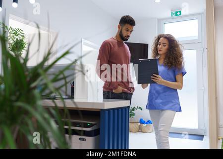 Junge Krankenschwester, die mit dem Patienten an der Rezeption in einer privaten Zahnklinik spricht. Stockfoto