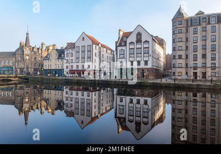 Leith, Edinburgh, Schottland, Großbritannien, 12.. Dezember 2022. Wetter im Vereinigten Königreich: Sonnenschein und Nebel. An einem bitterkalten Tag, an dem die Temperatur nicht über Null Grad steigt, scheint die Sonne auf das Wasser von Leith mit bunten Reflexionen der alten Gebäude im stillen Fluss. Kredit: Sally Anderson/Alamy Live News Stockfoto