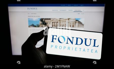 Person, die ein Mobiltelefon mit dem Logo des rumänischen Unternehmens Fondul Proprietatea S.A. auf dem Bildschirm vor der Unternehmenswebseite hält. Konzentrieren Sie sich auf das Display des Telefons. Stockfoto