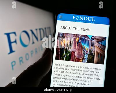 Person, die ein Mobiltelefon mit einer Website des rumänischen Unternehmens Fondul Proprietatea S.A. auf dem Bildschirm vor dem Logo hält. Konzentrieren Sie sich auf die Mitte des Telefondisplays. Stockfoto