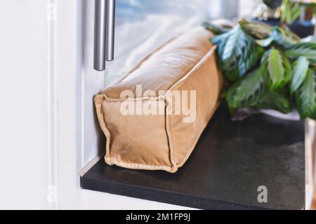 Zugluftstopper, der auf dem Fenster liegt, um kalte Luft fernzuhalten und Energie für die Heizung im Zimmer zu sparen Stockfoto