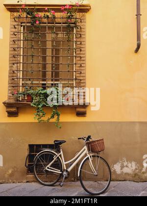 Ein weißes Fahrrad parkt neben einem gelben Gebäude unter einem eingezäunten Fenster Stockfoto