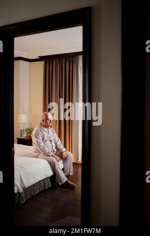 Unglücklicher alter Mann, der nach dem Aufwachen zu Hause im Bett sitzt Stockfoto