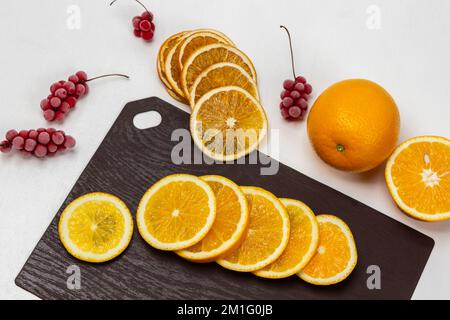 Scheiben frischer Orange auf einem Schneidebrett. Halb und ganz orange. Getrocknete Orangenscheiben. Strähnen gefrorener roter Beeren. Weißer Hintergrund. Flach l Stockfoto