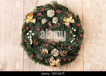 Blick von oben auf einen festlichen Weihnachtskranz mit goldenen Schleifen, Zapfen und roten Rowan-Beeren auf einem Holztisch Stockfoto