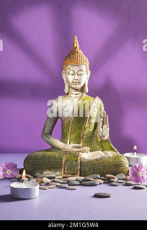 Grüne und goldene buddha-Statue in der Meditation mit Schatten auf hellem lila Hintergrund. Vertikales Format. Stockfoto