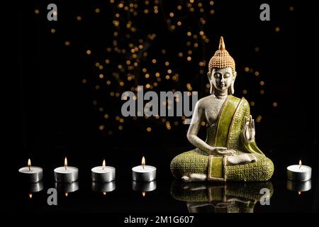 Buddha-Statue in der Meditation mit Lichtern und Kerzen auf schwarzem Hintergrund mit Kopierbereich. Stockfoto