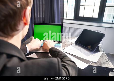 Ein Rückfahrbild eines unbekannten Geschäftsmannes, der auf seinem Laptop sitzt und tippt, mit einem Chromakey auf dem Hintergrund des Fensters. Mit Platz zum Kopieren. Hochwertiges Foto Stockfoto