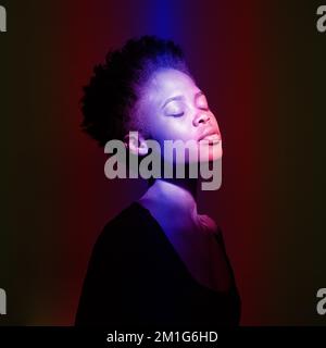 Junge, glückliche Afrikanerin im Studio. Ein weibliches Modell in bunten, hellen Neonlichtern posiert auf schwarzem Hintergrund. Das Konzept des künstlerischen Designs. Hochwertiges Foto Stockfoto