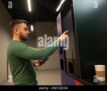 Ein weißer Mann wählt Kaffee in einem Selbstbedienungsautomaten. Stockfoto