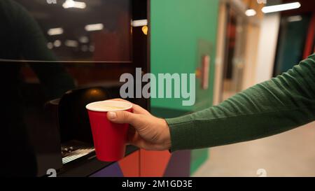 Ein weißer Mann gießt sich Kaffee aus einem Automaten ein. Schließen. Stockfoto