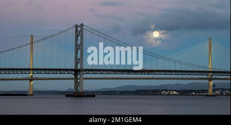 In Blue Hour, Firth of Forth, Schottland, Großbritannien, geht ein Vollmond über die Brücken Queensferry Crossing und Forth Road Stockfoto