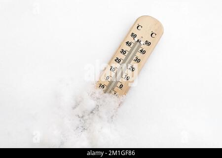 Holzthermometer auf Schnee zeigt niedrige Temperaturen unter Null in grad celsius an. Winterfrost. Wettervorhersagekonzept. Flach liegend, Draufsicht Stockfoto