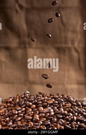 Kaffeebohnen fallen auf einen Berg gerösteter Kaffeebohnen. Stockfoto