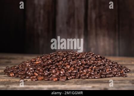 Ein kleiner Haufen gerösteter Kaffeebohnen auf einem alten Holztisch. Stockfoto