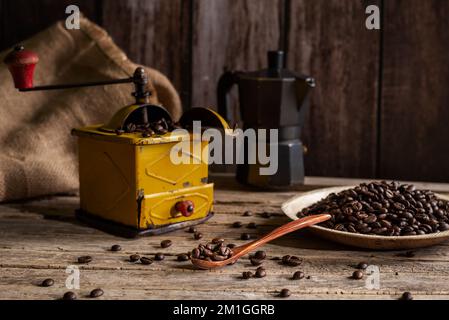Geröstete Kaffeebohnen auf einem Teller und in einem Holzlöffel neben einer alten Kaffeemühle zum Mahlen von Kaffee. Stockfoto