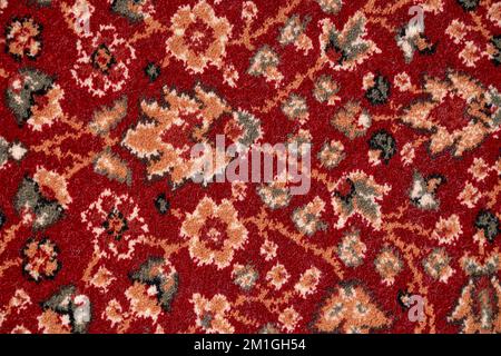 Nahaufnahme von Details komplexer Muster mit Blumenverzierung eines bunten Teppichs mit kurzem Flor. Textur aus rotem, kunstvoll verziertem persischen Teppich für Hintergrund, Fragment. Texturen und Hintergrund. Stockfoto