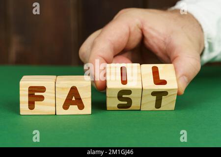 Geschäfts- und Bildungskonzept. Auf einer grünen Oberfläche legt ein Mann Würfel mit der Inschrift - SCHEITERN, SCHNELL Stockfoto