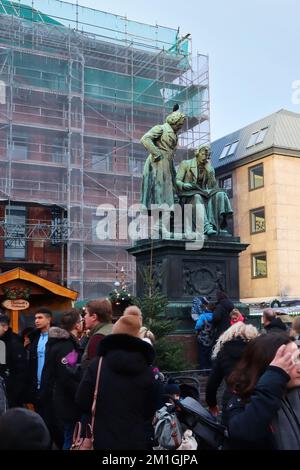 Hanau, Deutschland - 15. Dezember 2019: Licht trifft die Brüder-Grimm-Statue mit einem Vogel auf dem Kopf während eines Weihnachtsmarkts in Hanau. Stockfoto
