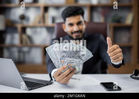 Portrait eines glücklichen jungen, attraktiven männlichen Buchhalters, der Bargeld in der Hand hält und Geld in einem modernen Büro zählt. Konzept der Finanzplanung und Mittelzuweisung. Stockfoto