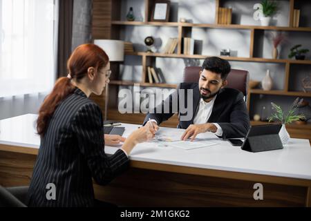 Rückansicht von zwei Geschäftsleuten, Mann und Frau, die die Seiten des Vertrags vertreten und sich während des Gesprächs im Büro am Tisch gegenübersitzen und über das Geschäft sprechen. Stockfoto
