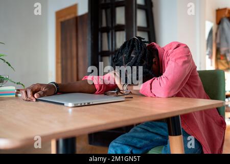 Erschöpfter, überlasteter Afrikaner, Fernarbeiter, der auf dem Schreibtisch schläft, leidet an einem Burnout von Freiberuflern Stockfoto