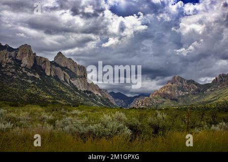 Wunderschöne Wolken und Gipfel der wilden, abgelegenen Chiricahua Mountains in Arizona. Stacheldrahtzaun im Vordergrund erzeugt metaphorischen Kontrast. Stockfoto