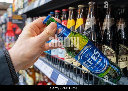 Die Hand des Mannes hält Efes Bierflasche aus dem Regal des Supermarkts. Verschiedene Bierflaschen im Regal. Minsk, Belarus, 2022 Stockfoto