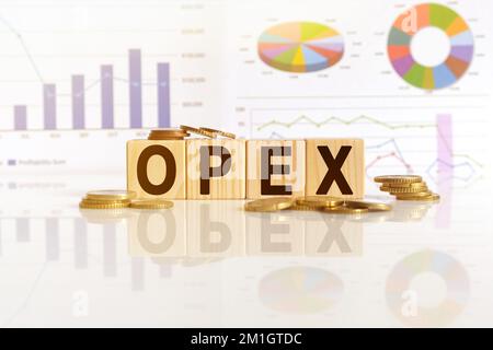 OPEX das Wort Holzwürfel, Würfel stehen auf einer reflektierenden Oberfläche, im Hintergrund ist ein Geschäftsdiagramm. Geschäfts- und Finanzkonzept Stockfoto